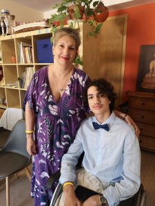 Imagen de Julia Herrera y Pol, su hijo, ella está de pie, con un vestido morrado con blanco, el está sentado con una camisa azul claro y corbata de moño negra, julia tiene cabello corto entrecano, pol tiene cabello negro, 